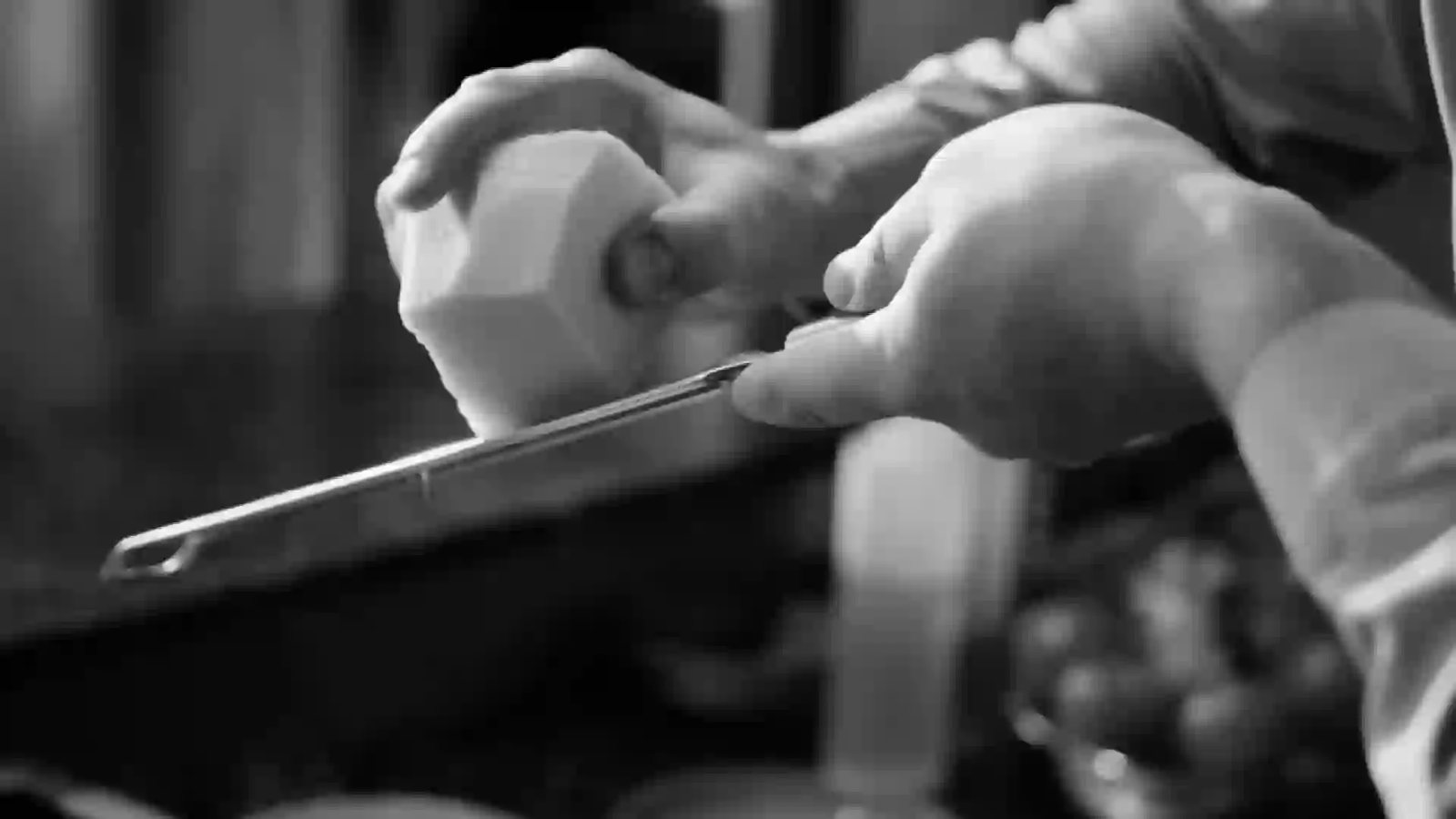 Close-up, in black and white, of a pair of hands working in a kitchen.
