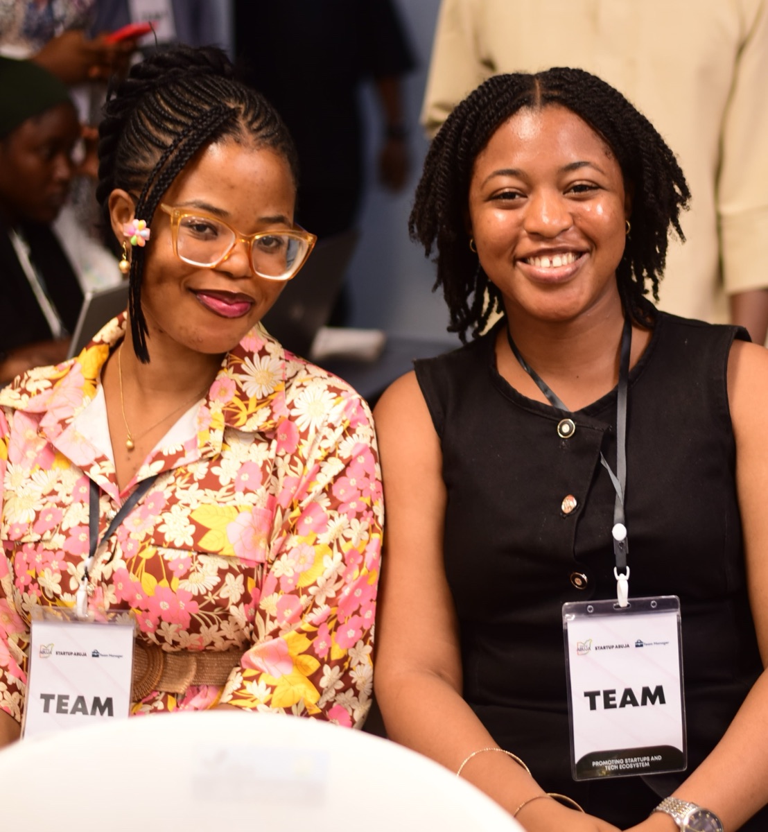 Two members of the Startup Abuja team, wearing team lanyards, smiling at an event.