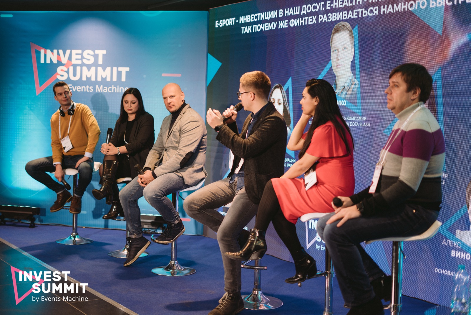 Six speakers on bar stools on a blue-lit stage under an Invest Summit screen, with Alex Vinogradov in a striped sweater at the far right.